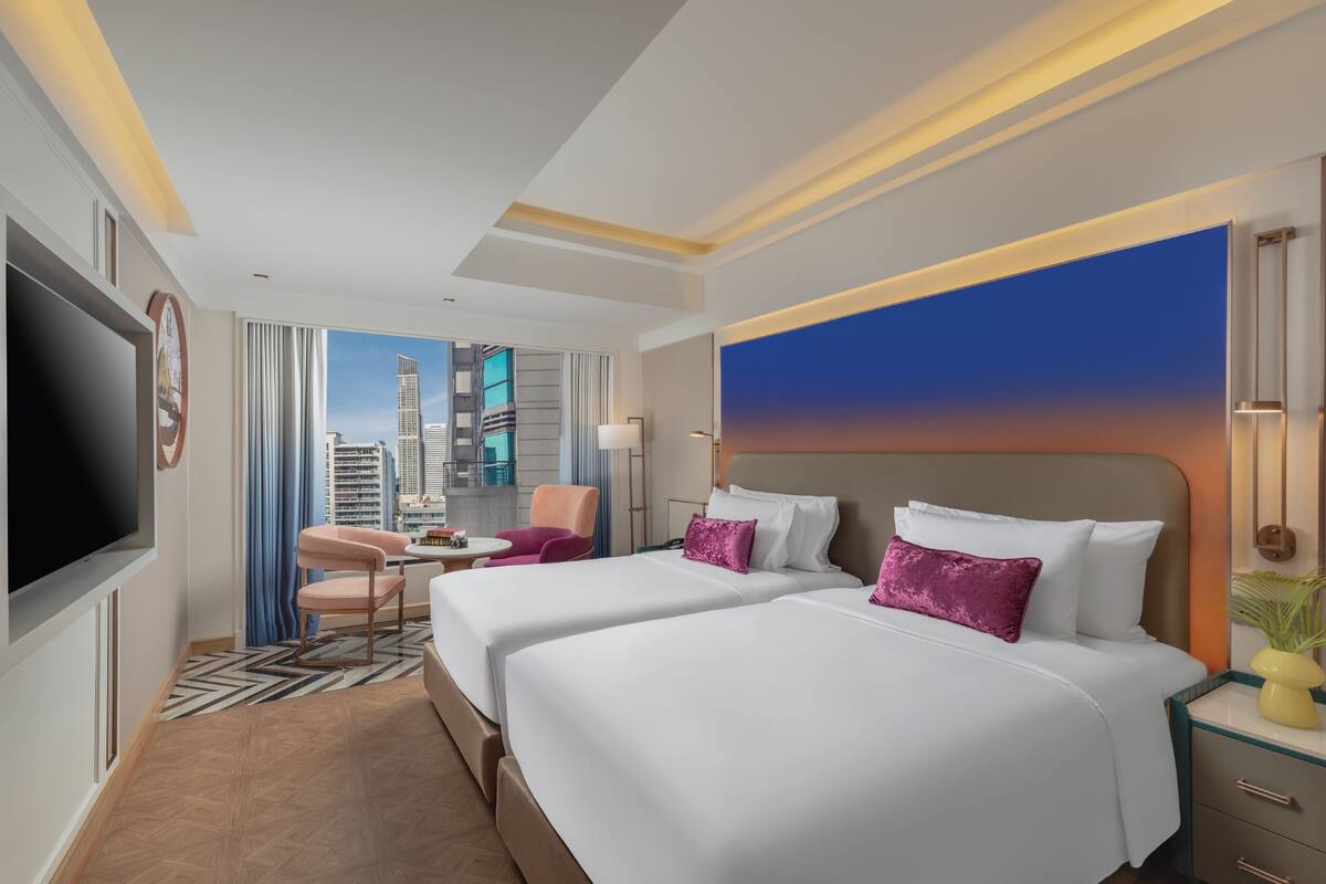 A hotel room with two beds, a TV, a desk, and a view of the cityscape.