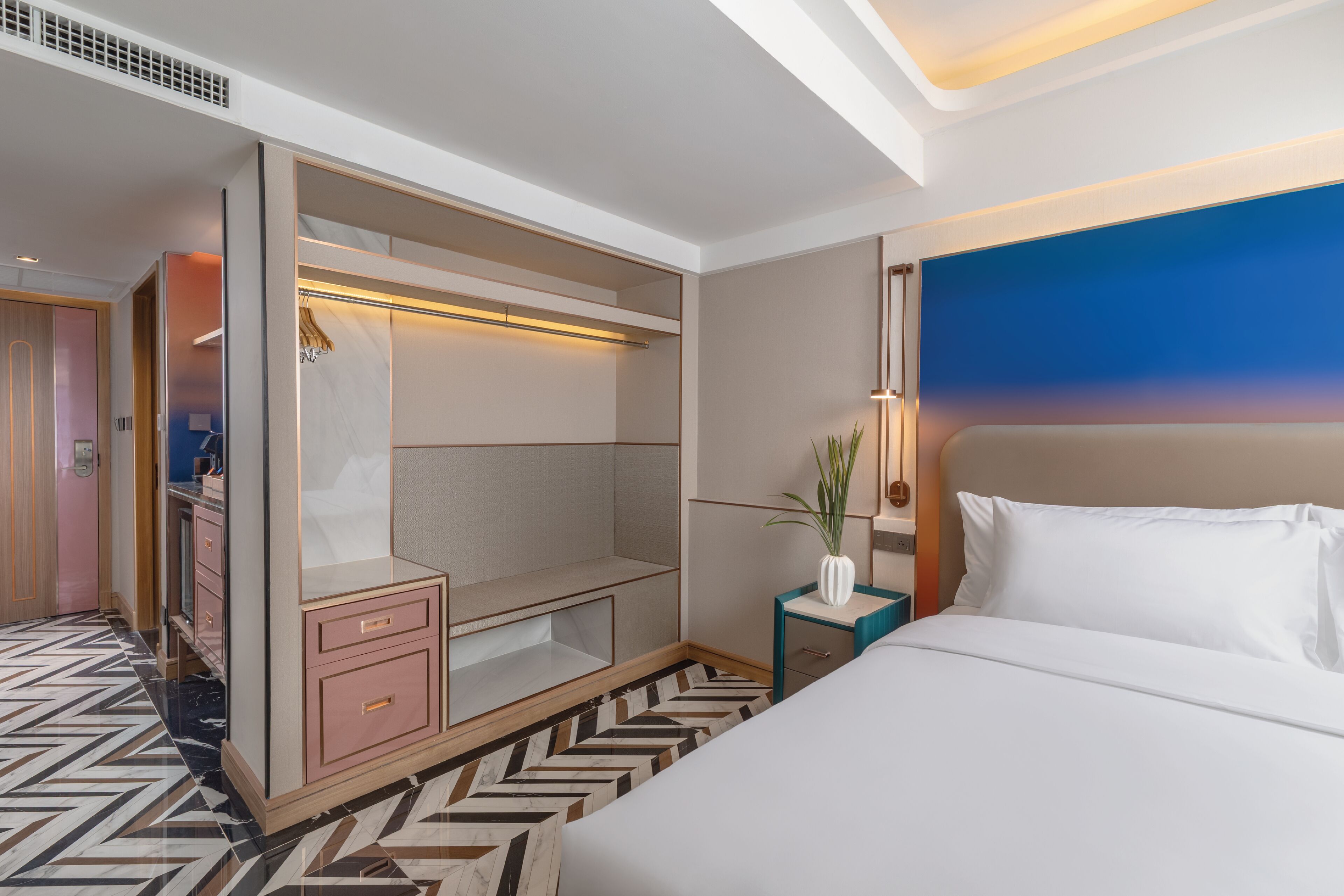 Une chambre d’hôtel dotée d’un grand lit, d’un dressing, d’une table de chevet avec une lampe et offrant une vue sur le panorama de la ville.