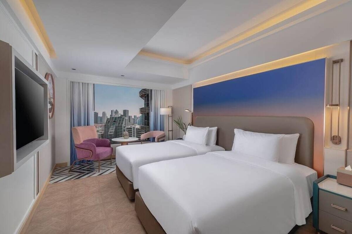 A hotel room with two beds, a cityscape view, a television, and a desk with a chair.