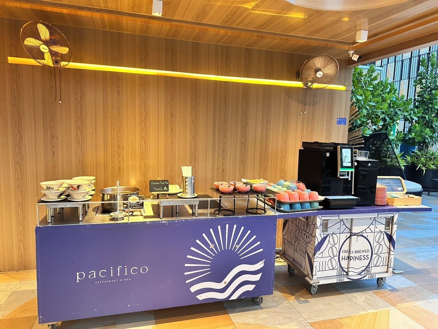 A cafe setup with a menu board, a coffee machine, and a cart with beverage containers.