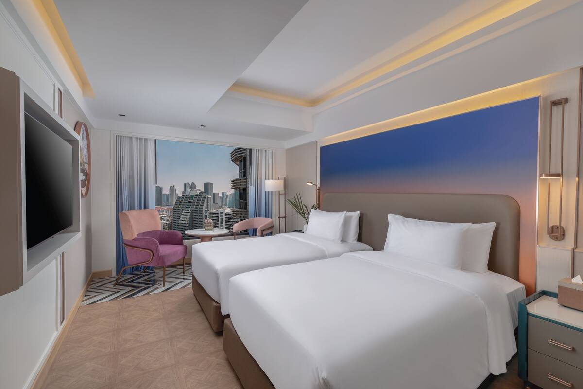 A hotel room with two beds, a TV, a city view, a desk, and a chair.