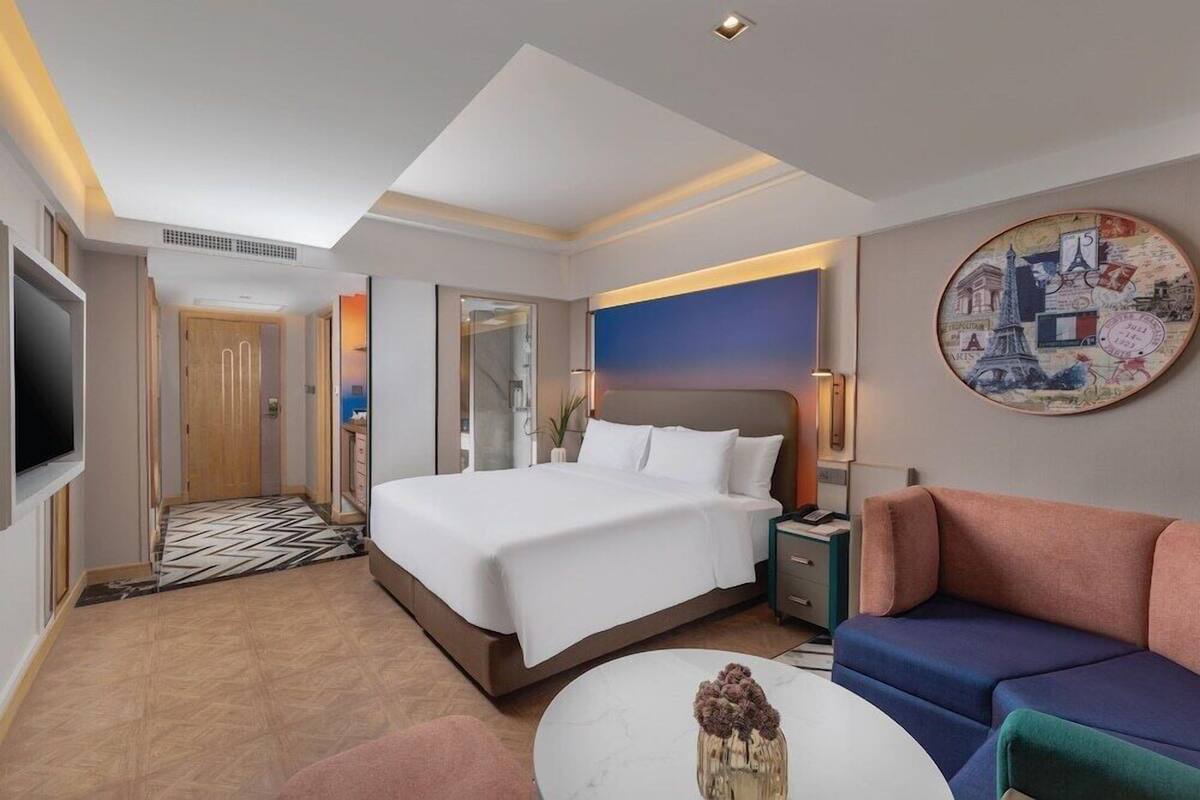 A hotel room with a bed, a sofa, a TV, a painting, and a decorative vase.