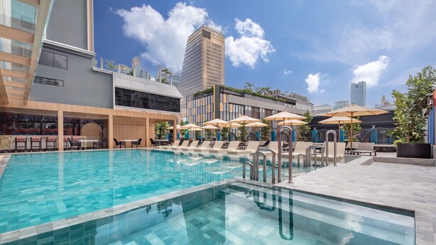 A swimming pool with lounge chairs and umbrellas, surrounded by modern buildings and a clear sky. - Pipa Bangkok Sukhumvit 11 by Kingston Hotels (Bangkok)