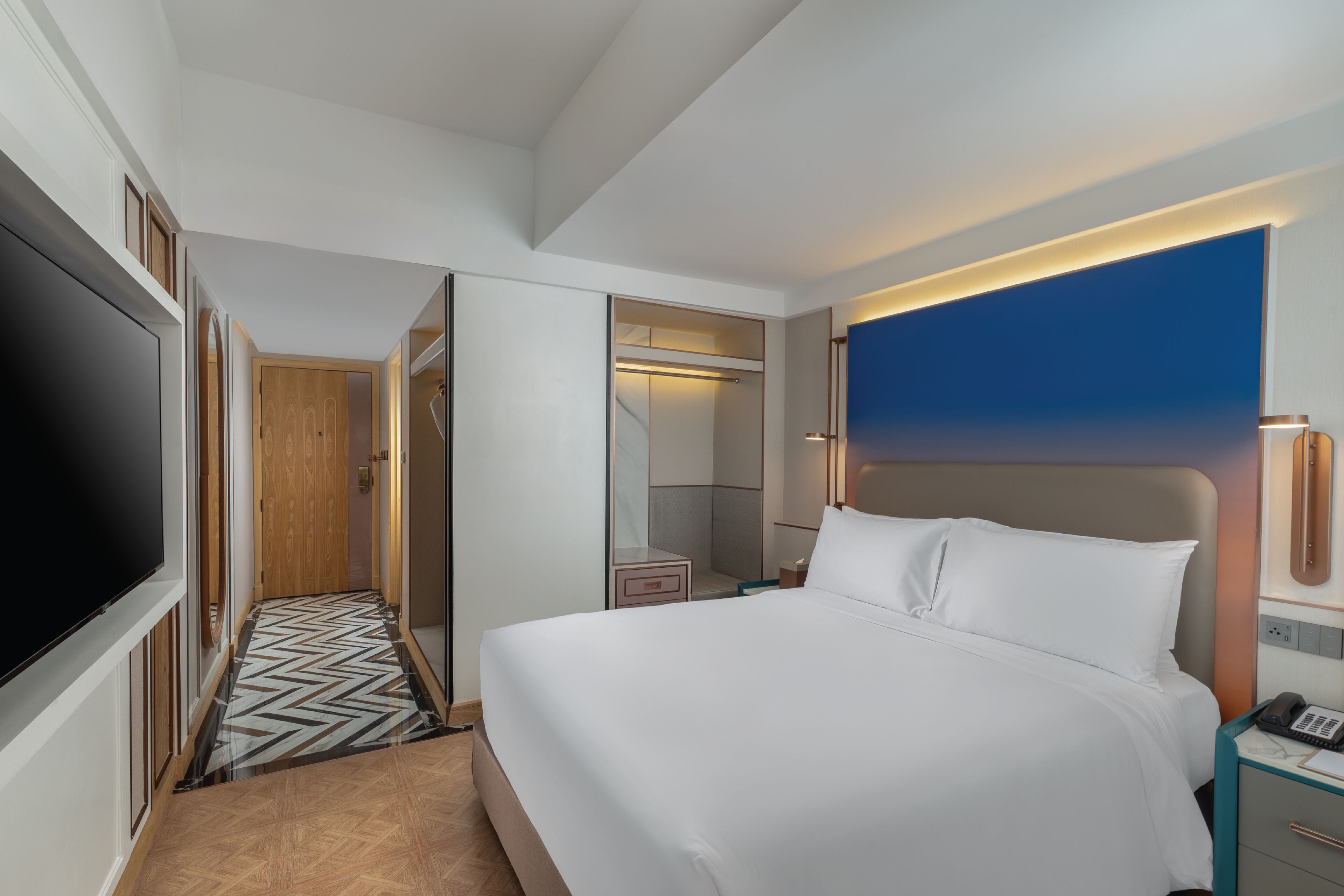 A hotel room with a large bed, a TV, a walk-in closet, and a bathroom with a mirror.