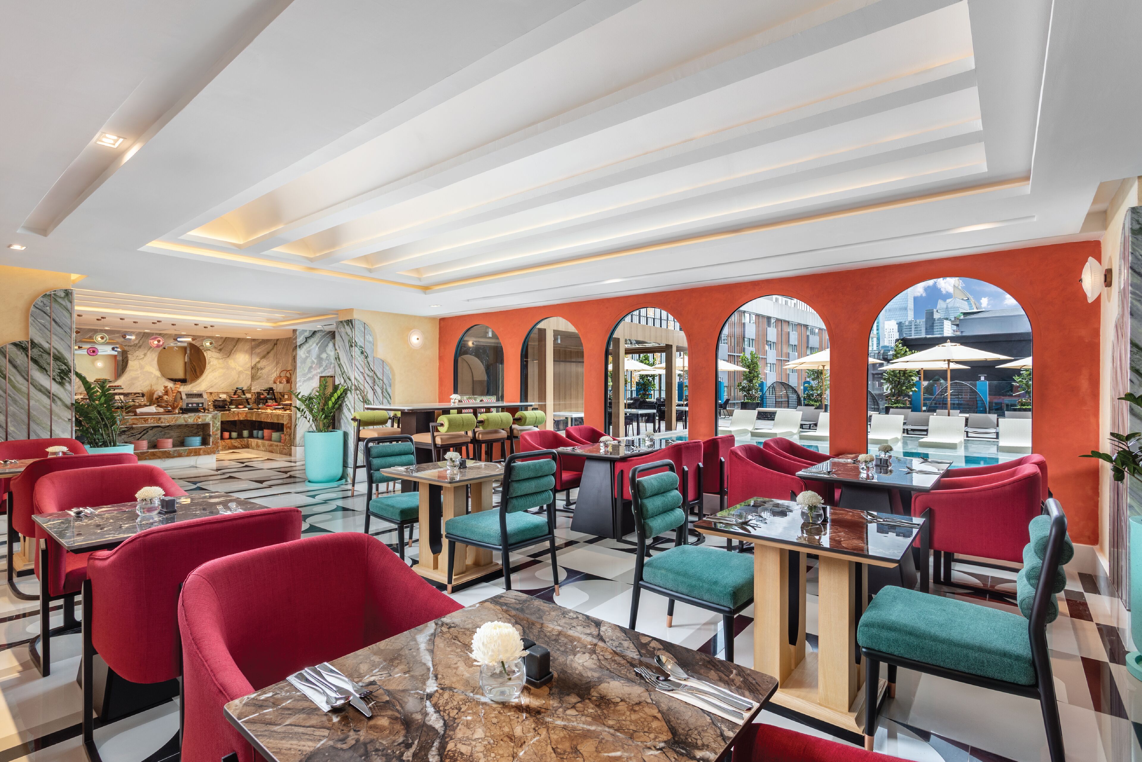 Un restaurante moderno con sillas rojas y turquesas, mesas de mármol y grandes ventanales con vistas a la ciudad.