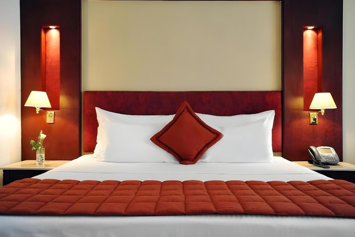 A hotel room with a large bed, two bedside lamps, a telephone, and a decorative vase.