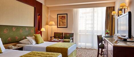 A hotel room with two beds, a desk with a television, a chair, and a desk lamp.