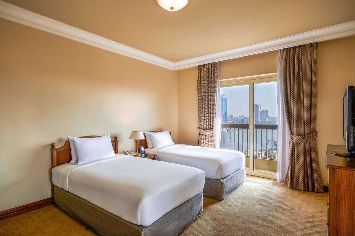 A hotel room with two beds, a city view, a balcony, and a television.