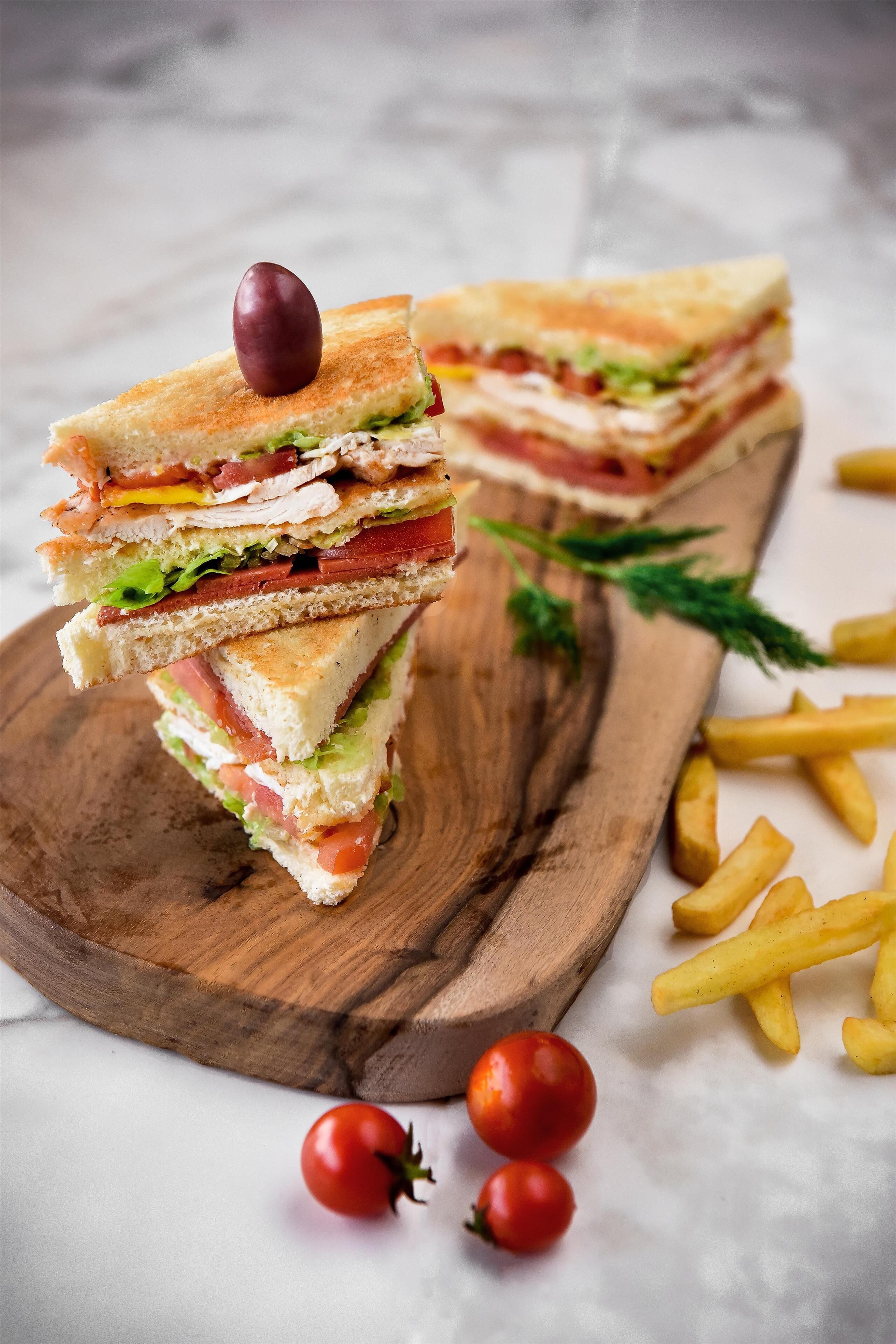 A sandwich on a wooden board with fries and tomatoes.