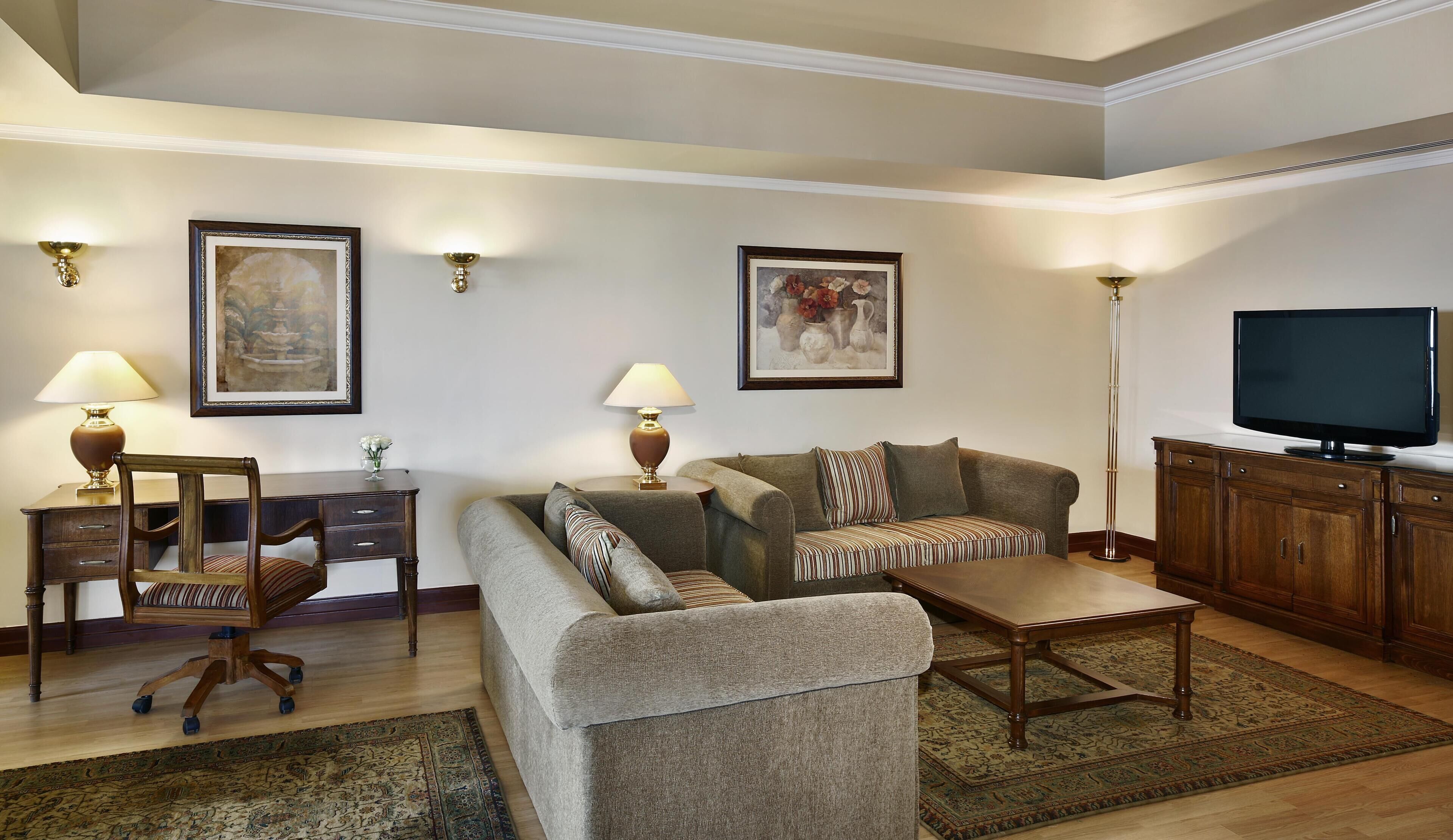 A living room with a sofa, armchair, coffee table, TV, and decorative lamps.