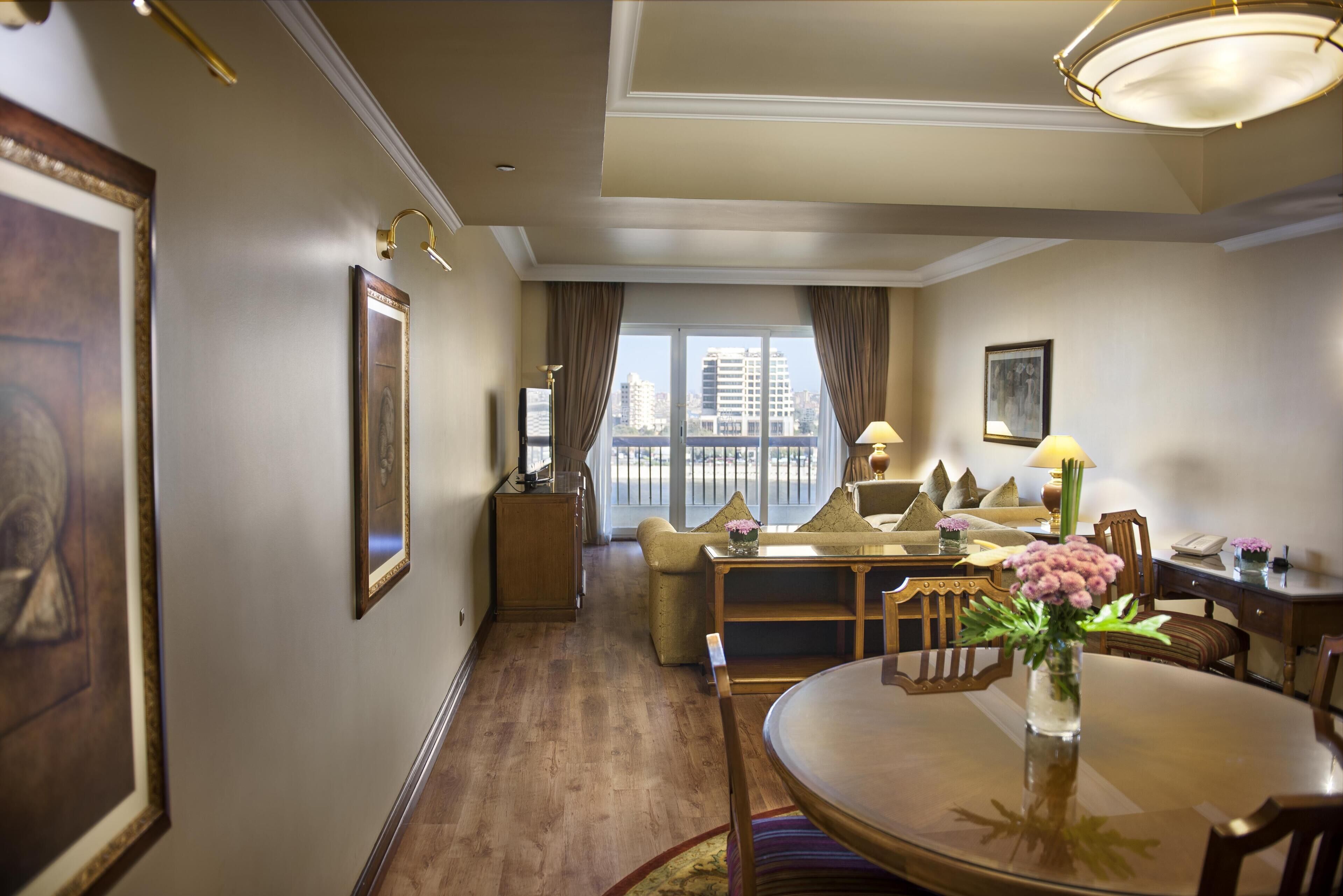 Habitación de hotel con comedor, sofá, vista a la ciudad y obras de arte enmarcadas en las paredes.