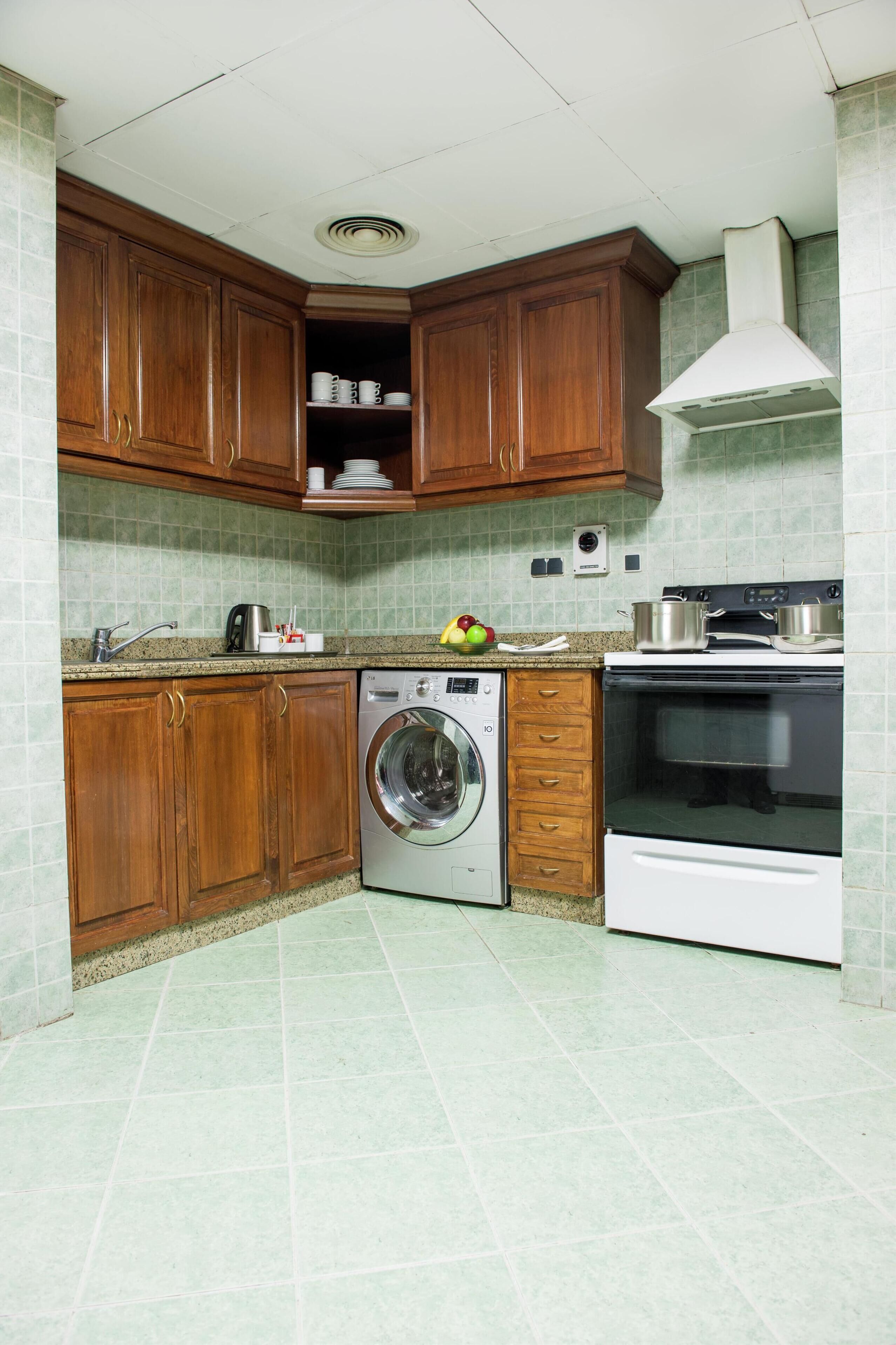 A kitchen with wooden cabinets, a washing machine, an oven, and a tiled backsplash.
