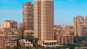 A high-rise hotel with multiple floors, a prominent sign at the top, and a view of the surrounding cityscape and water. - Hilton Cairo Zamalek Residences (Cairo)