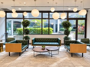 A modern lounge area with a green sofa, two armchairs, a coffee table, and pendant lighting. - YWCA Fort Canning (Singapore)