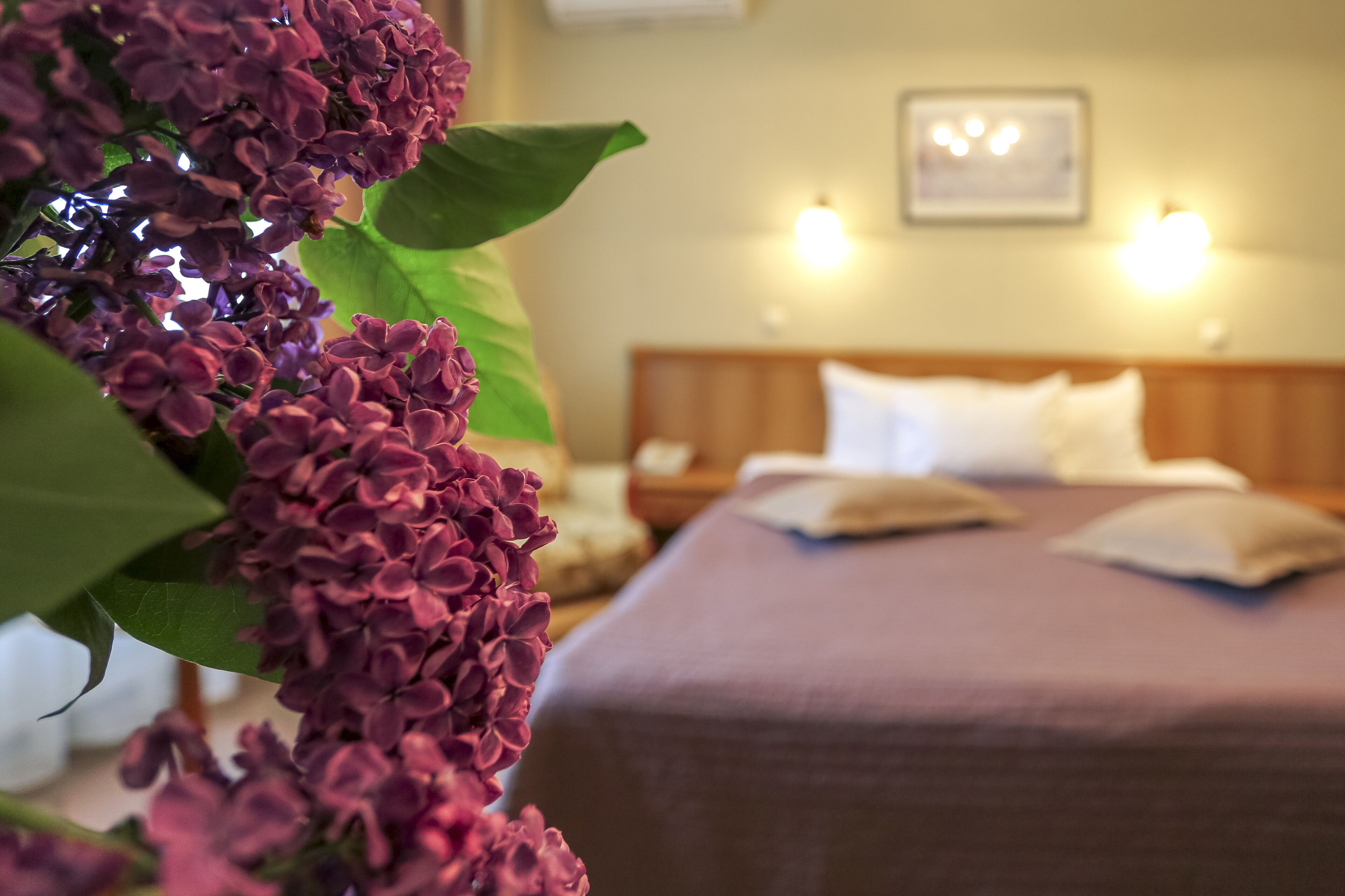 A hotel room with a bed, pillows, a nightstand, and a wall-mounted light fixture.
