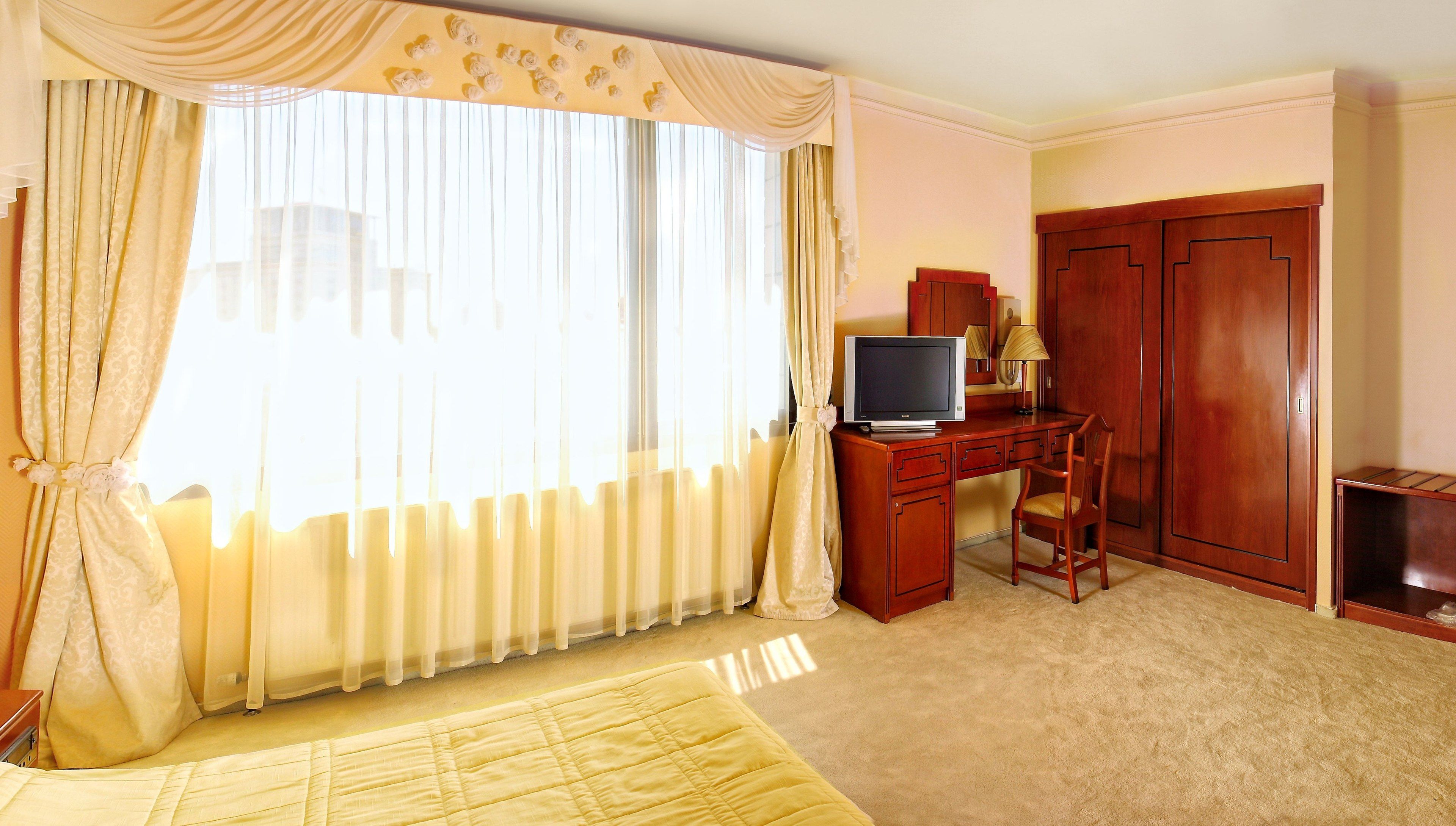 A hotel room with a bed, a desk with a television, a wardrobe, and curtains.