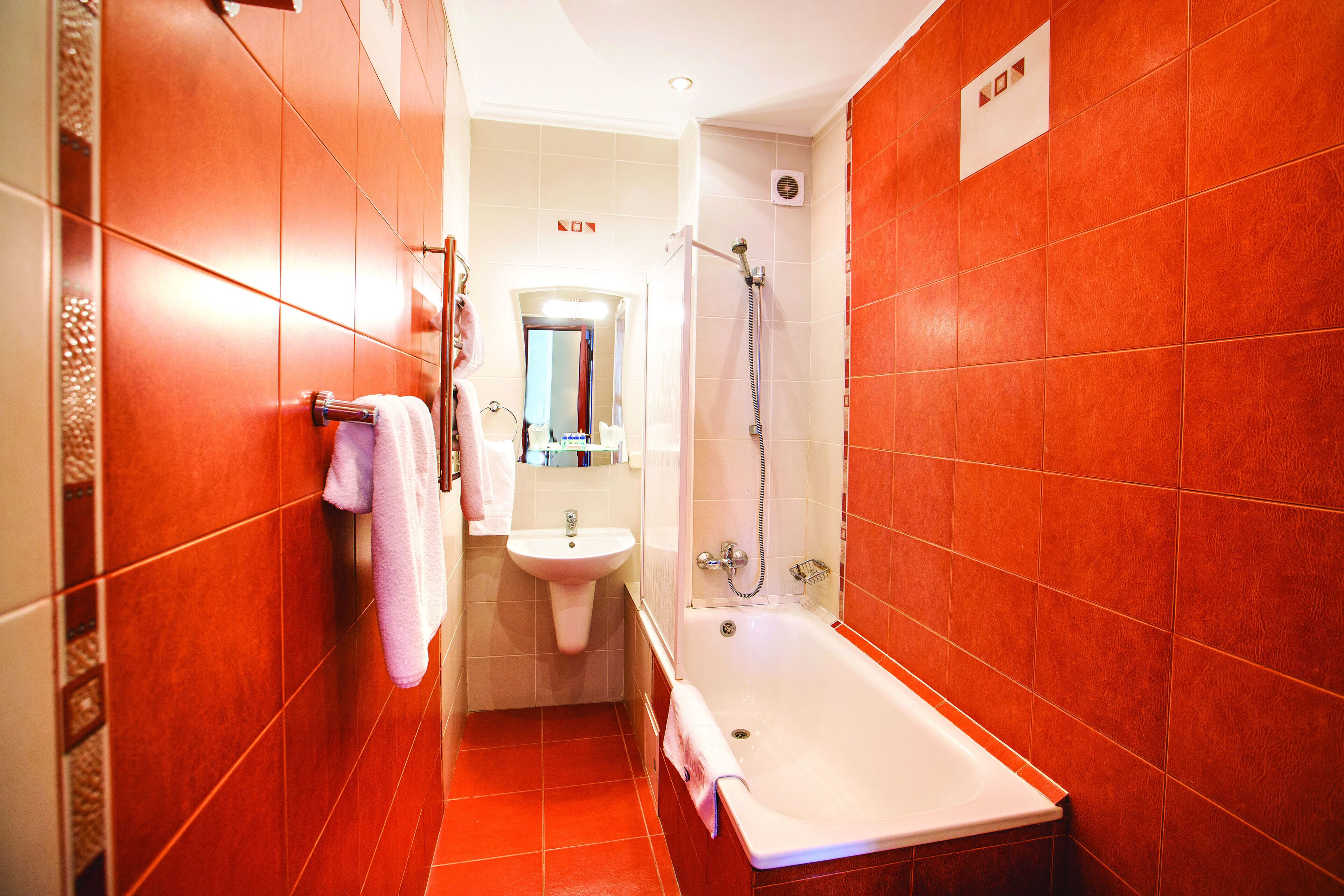 Une salle de bain avec des carreaux rouges, un lavabo, un miroir et une baignoire.