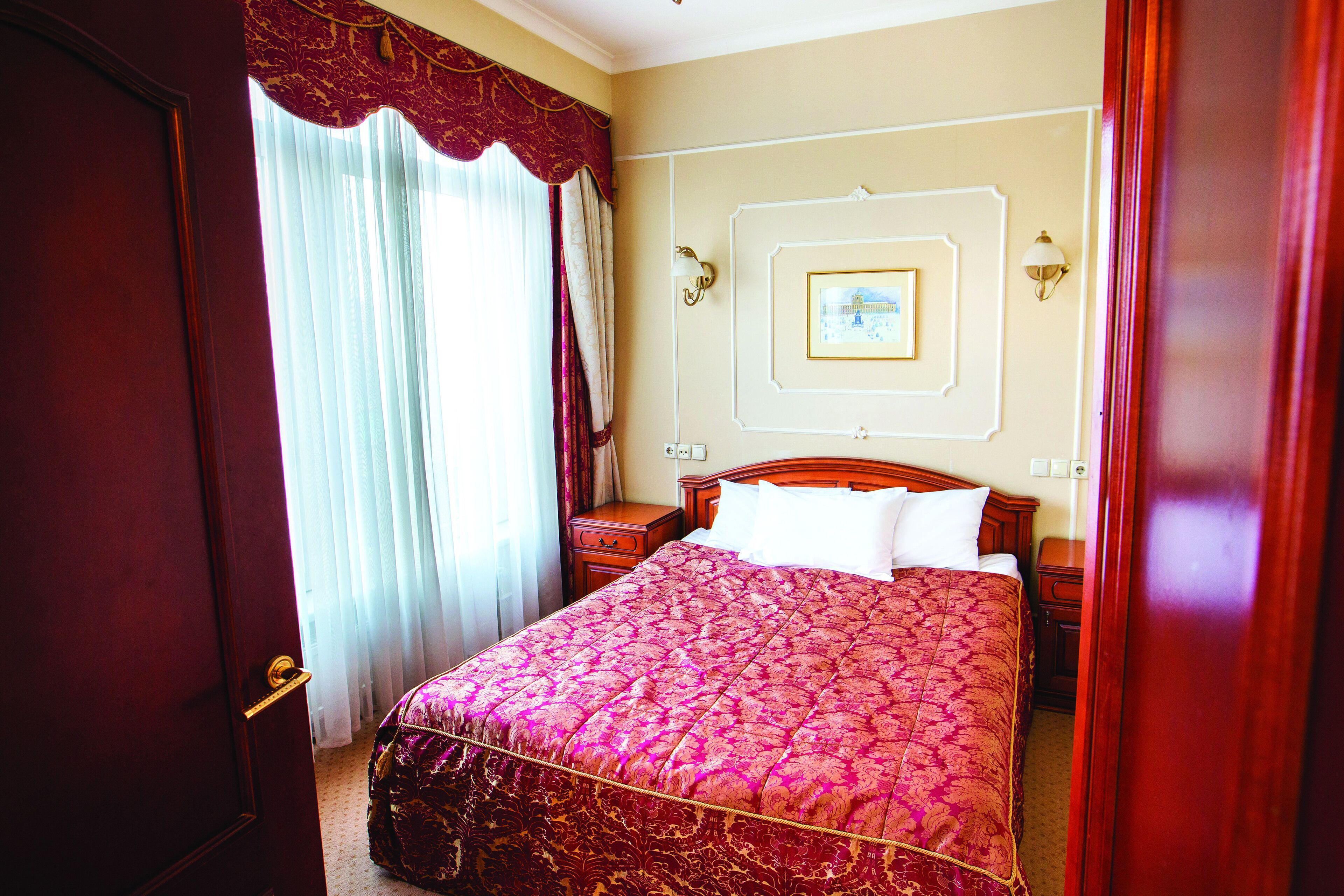 Une chambre d’hôtel avec un grand lit, une table de chevet en bois, une lampe fixée au mur et un tableau encadré.