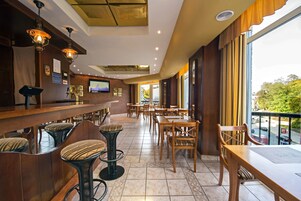 Un restaurante con zona de bar, mesas y sillas altas. Hay un televisor montado en la pared y vistas al exterior a través de amplias ventanas.