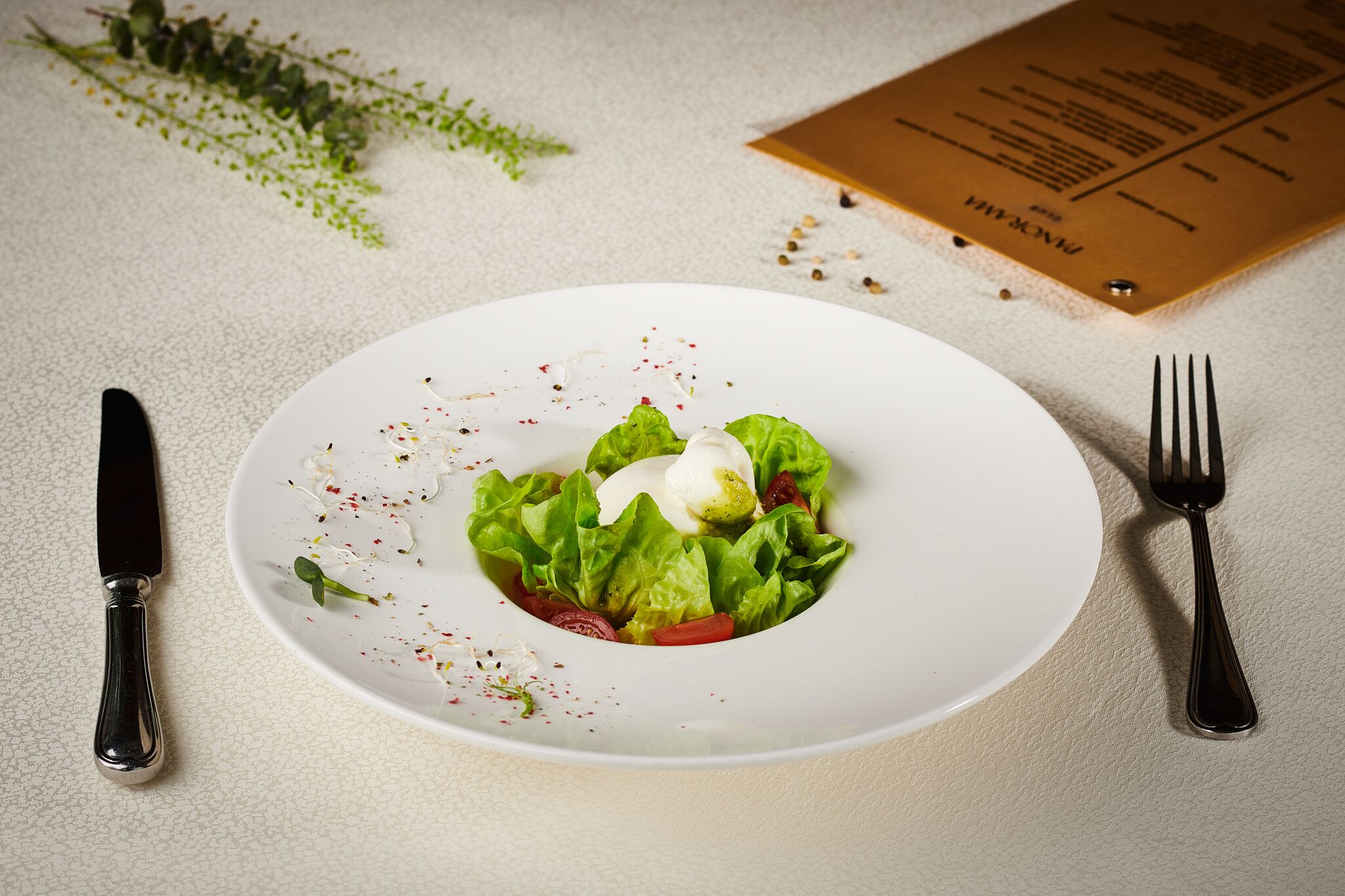 Un plato blanco con una ensalada, un tenedor y un cuchillo sobre una superficie texturizada.