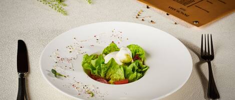 Un plato blanco con una ensalada, un tenedor y un cuchillo sobre una superficie texturizada.