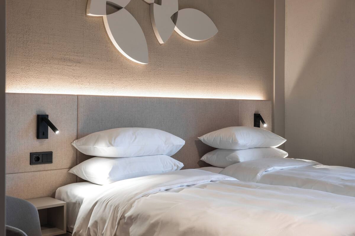 A modern hotel room with a large bed, a wall-mounted light fixture, and a side table.