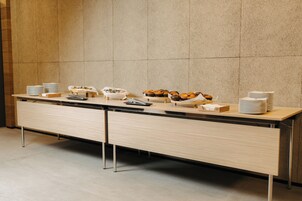 Una mesa de buffet con platos, tazones y una bandeja de muffins frente a una pared con azulejos.