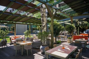 An outdoor patio area with wooden tables and chairs, potted plants, and a view of the street. - Mimi Hotel Chisinau (Chisinau)