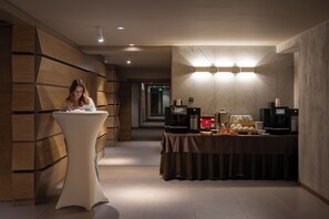 Un pasillo moderno de hotel con mostrador de recepción, zona de buffet con máquinas de café y un diseño de pared de madera.