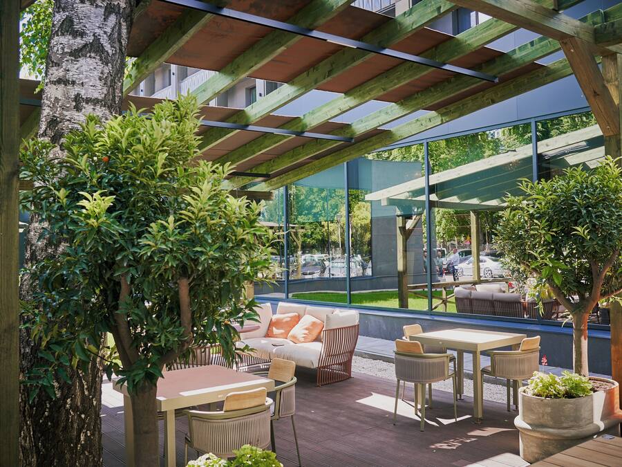 An outdoor seating area with wooden tables and chairs, a cushioned sofa, and potted plants.