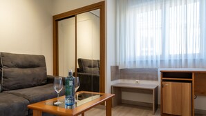 Een knus woongedeelte met een bank, een glazen tafel met fles en glas, een klein houten bureau en een kast.