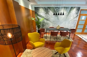 Un salón de conferencias con suelo de madera, una mesa redonda y sillas amarillas. Hay un ventanal con vistas a árboles y una pared con un diseño texturizado.