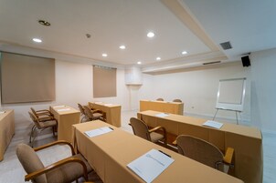 A conference room with beige tables, chairs, a whiteboard, and a projector screen.
