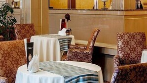 Eine Hotellobby mit Empfangsschalter, mehreren Sitzbereichen mit gemusterten Stühlen und einer Wand mit Uhren.
