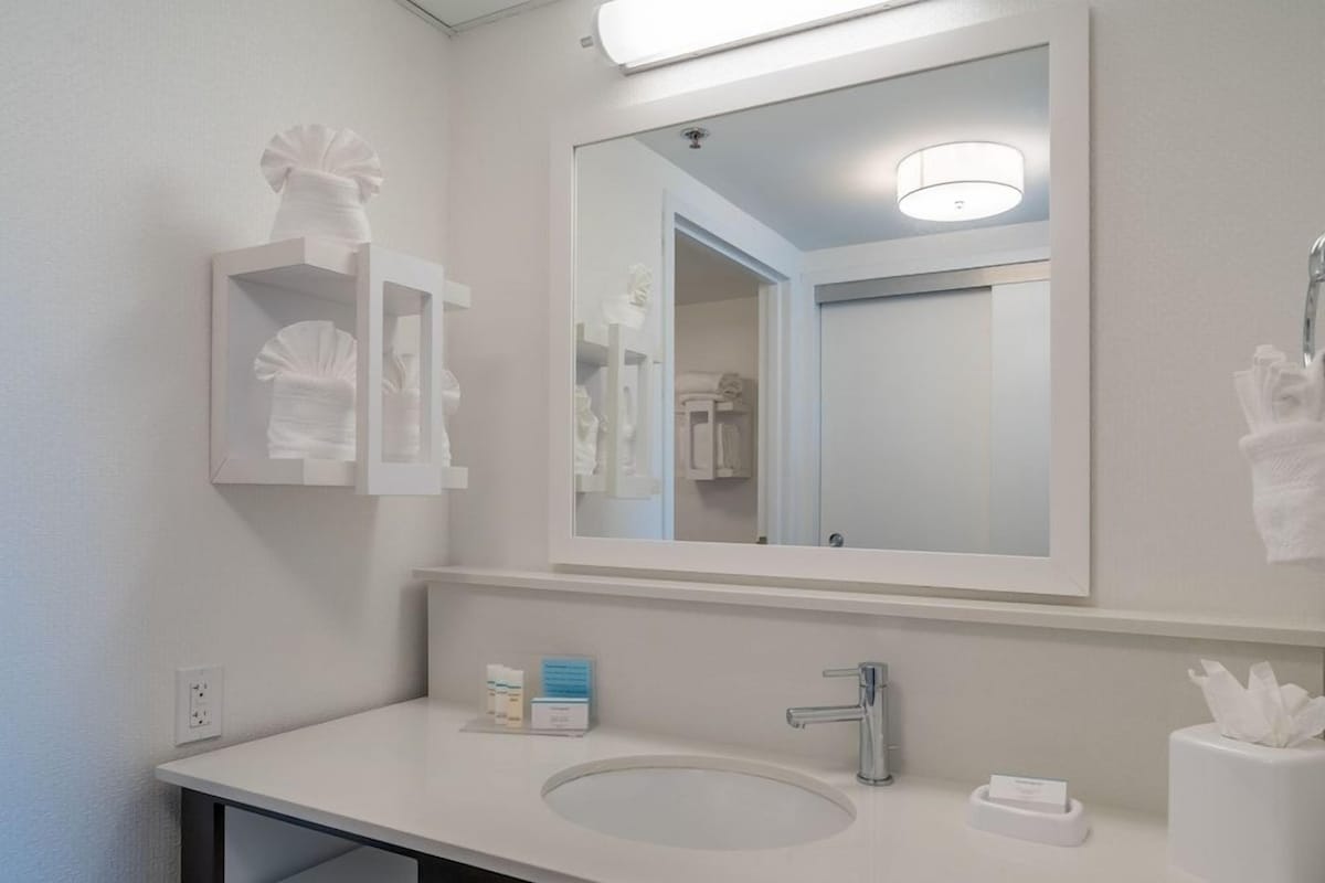 A bathroom with a large mirror, a sink, and a towel rack.