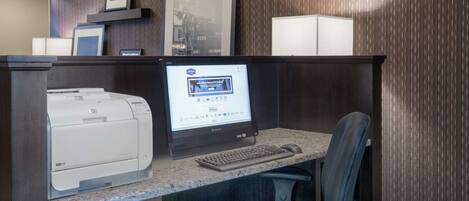 Un mostrador de recepción de hotel con una computadora de escritorio, una impresora y una silla.