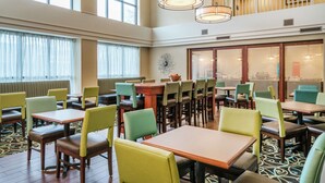 A dining area with multiple tables and chairs, a large window, and a staircase leading to an upper level. - Hampton Inn & Suites Valley Forge/Oaks (Phoenixville)