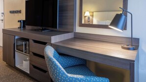 A modern hotel room with a flat-screen TV, a desk with a lamp, a patterned chair, and a minibar. - Hampton Inn & Suites Valley Forge/Oaks (Phoenixville)