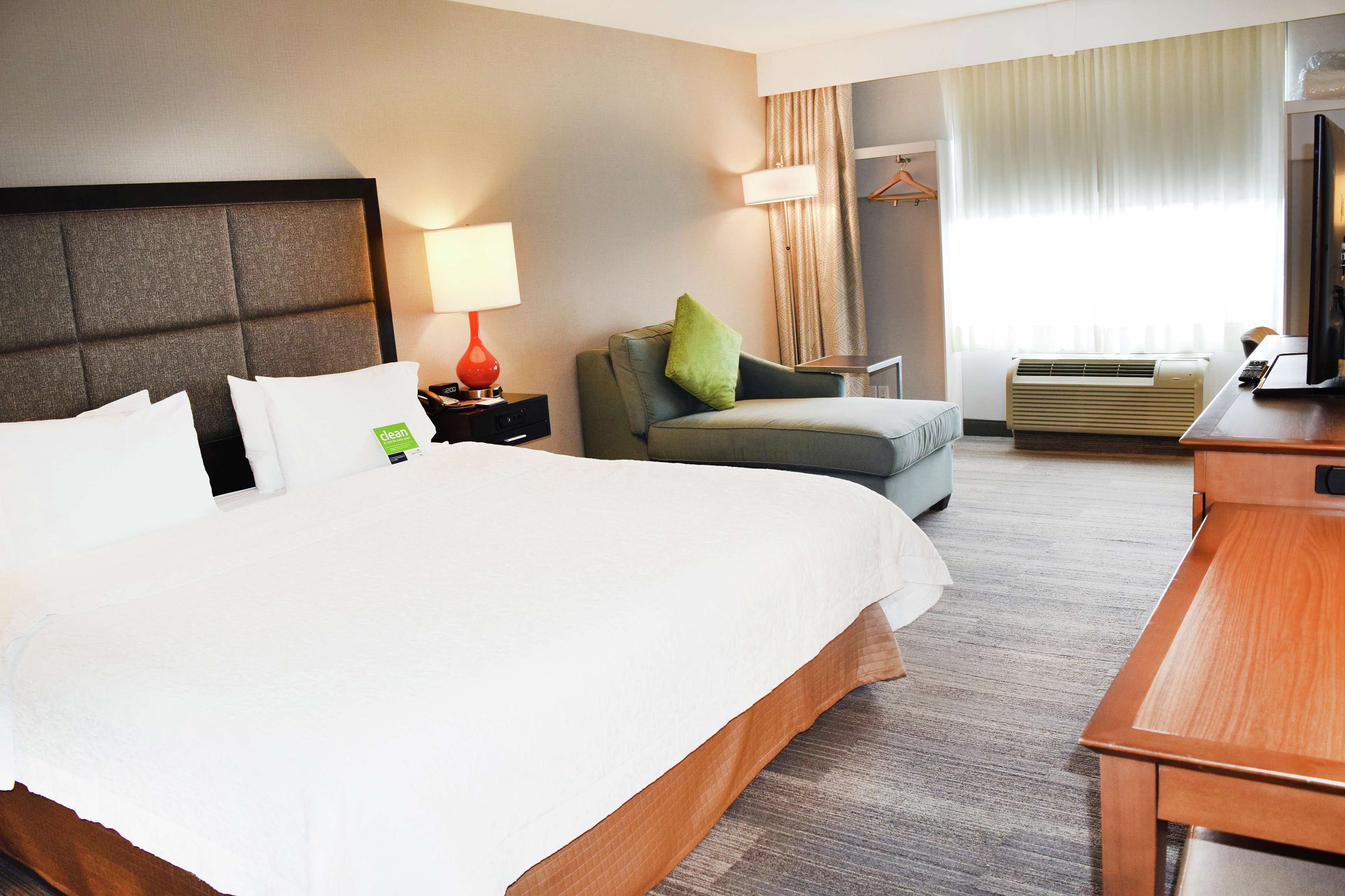 Une chambre d’hôtel avec un grand lit, un bureau, une chaise, une lampe et un appareil de climatisation.