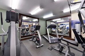 Une salle de sport équipée de divers appareils d’exercice, notamment des tapis de course et des appareils de musculation, et dont les murs sont recouverts de miroirs.