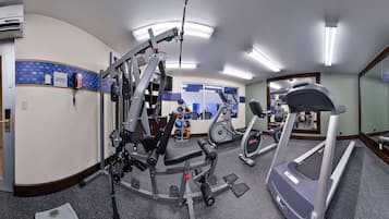 Un gimnasio con equipo de cardio, máquinas de pesas y un espejo grande.