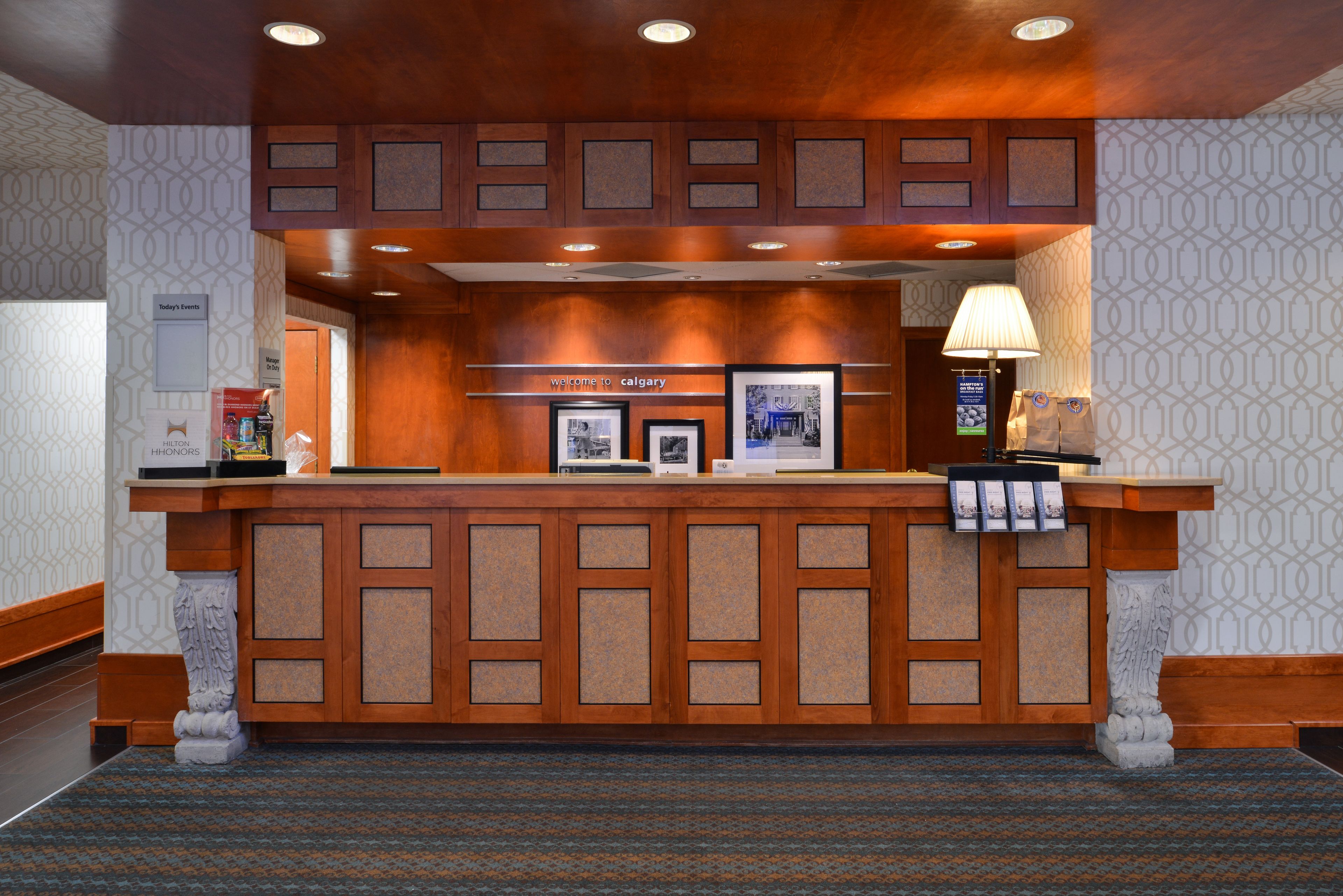 A reception desk with a wooden finish, a framed welcome sign, and a lamp.