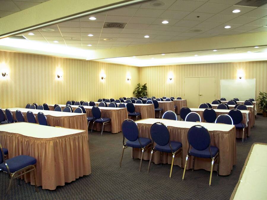 A conference room with multiple tables and chairs, equipped with overhead lighting and a whiteboard.