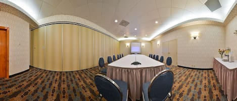 Une salle de conférence avec une longue table, des chaises, un écran de projection et une petite table ornée de fleurs.