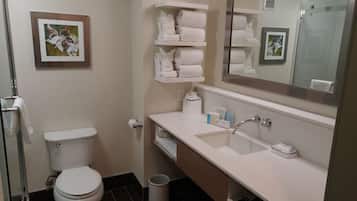 Un baño con inodoro, lavamanos con espejo y repisas con toallas.