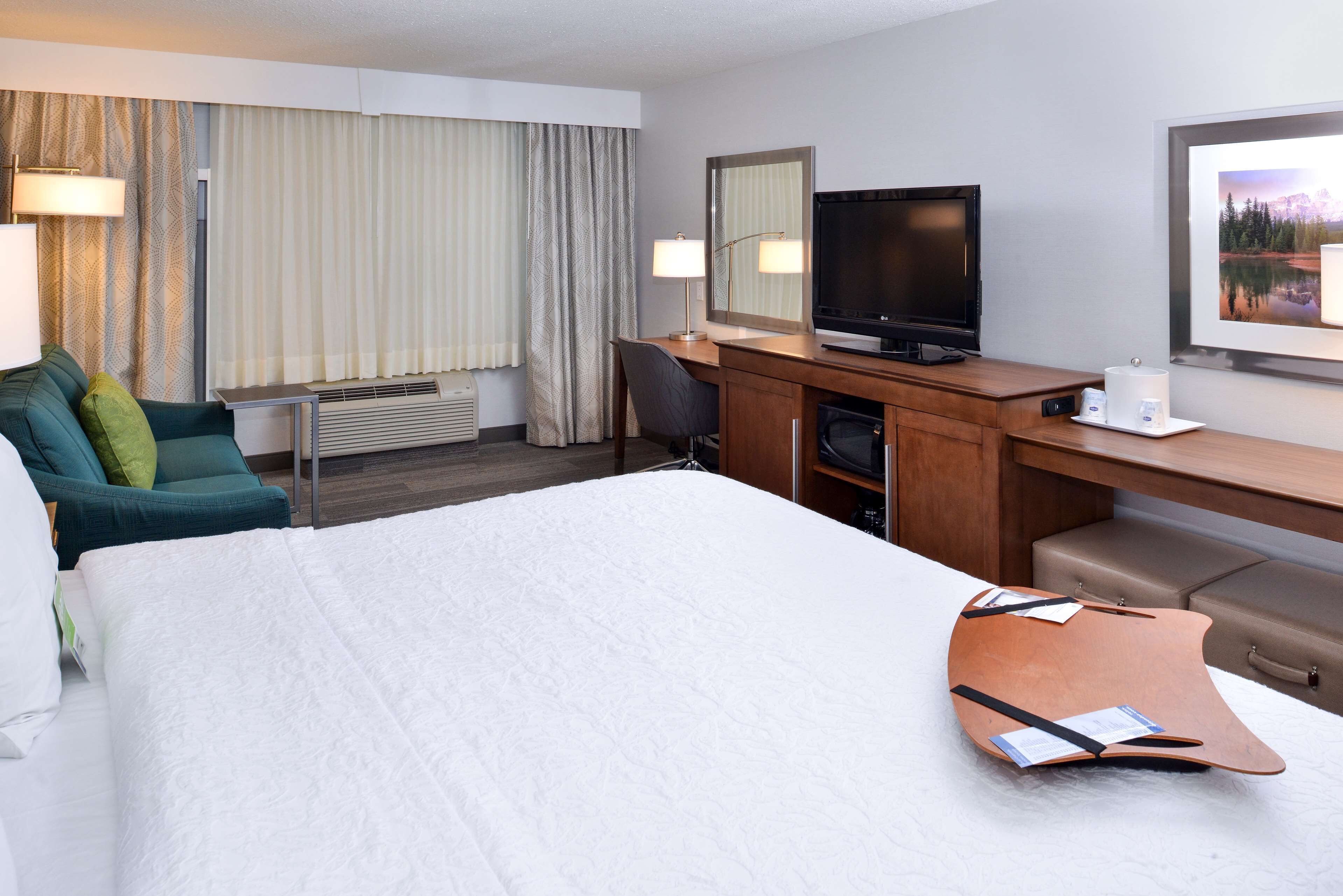 Una camera d'albergo con un letto, una scrivania, una televisione, una sedia e una finestra con tende.