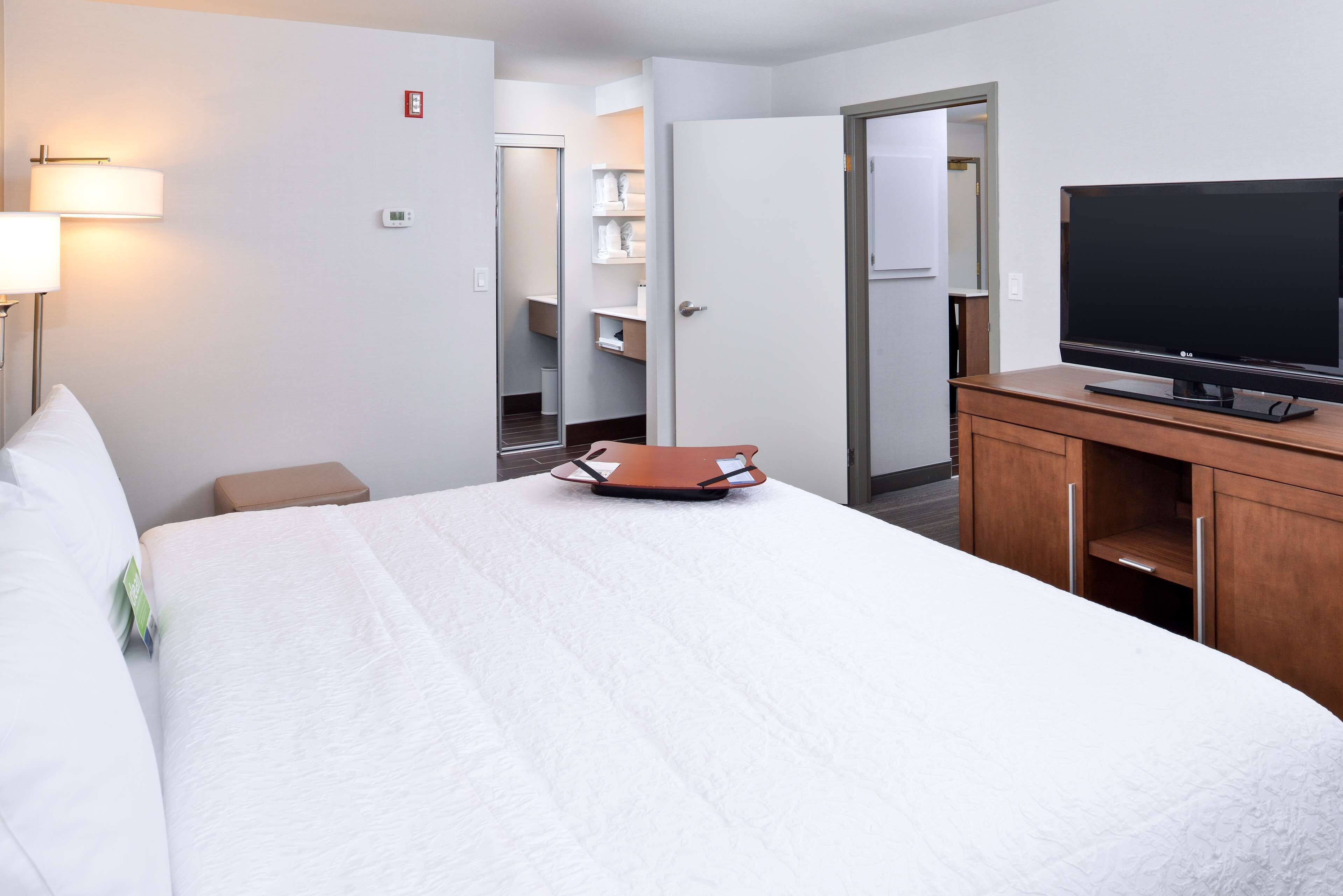 A hotel room with a bed, a TV on a wooden stand, a bedside table, and a closet with shelves.
