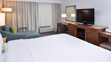 Une chambre d’hôtel avec un grand lit, un bureau avec une télévision, une chaise, une lampe de bureau et une fenêtre avec des rideaux.