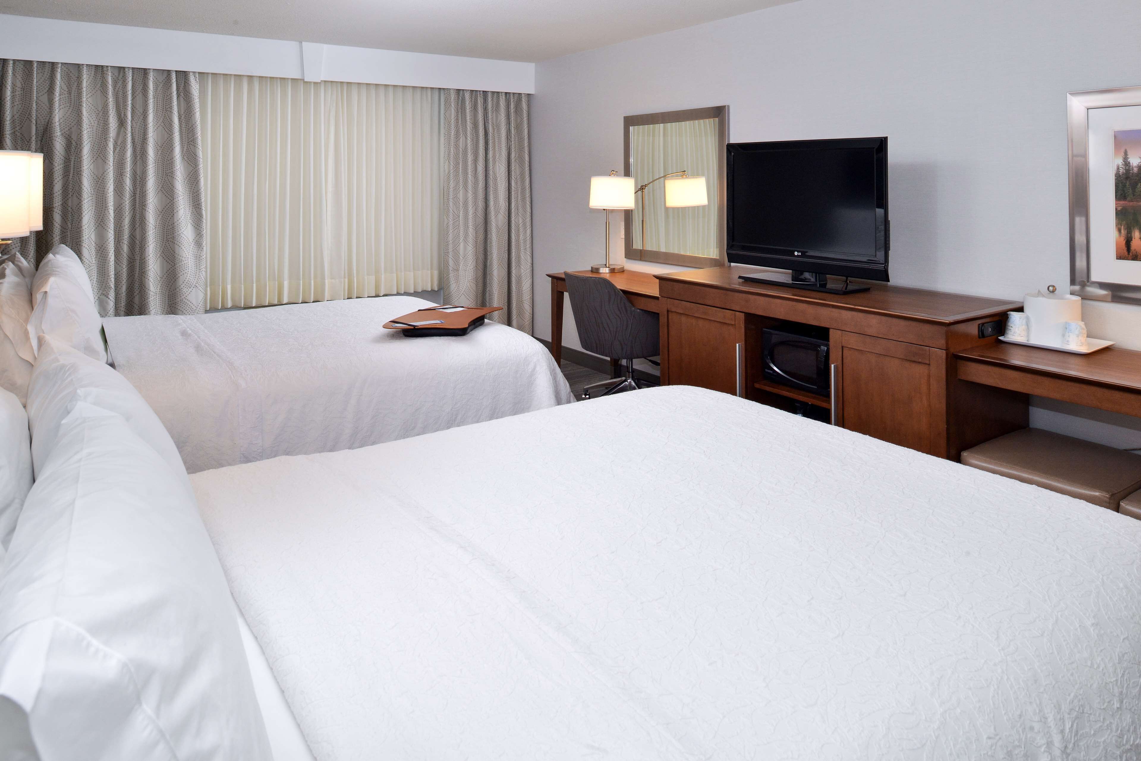 A hotel room with two beds, a desk with a TV, a lamp, and a mirror.
