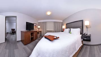 A hotel room with a large bed, a desk with a television, a wardrobe, and a bathroom visible through an open door.